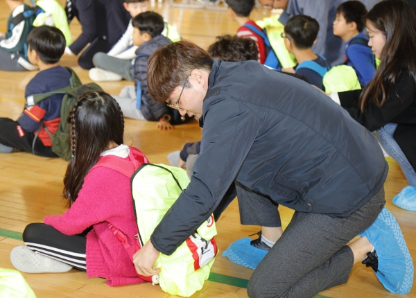 현대위아의 한 직원이 18일 경상남도 창원시 삼정자초등학교에서 한 학생의 가방에 교통사고 예방에 도움을 주는 ‘교통안전 가방덮개’를 씌우고 있다. (사진=현대위아)