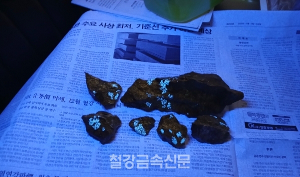우성금속이 채굴한 구리 원광을 미네랄 라이트(Mineralight)로 비춘 모습. 형광색을 띠는 부분은 텅스텐이다. 해당 원광에는 구리 외에도 금과 은, 텅스텐이 함유되어 있다. (사진=철강금속신문)
